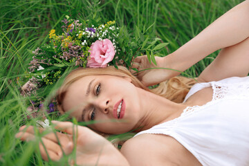 Young woman wearing wreath made of beautiful flowers on green grass