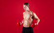 © Prostock-studio - Aggressive young sportsman in boxing gloves screaming in anger on red studio background