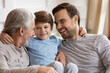 © fizkes - Close up happy three generations of men hugging, having fun, cute adorable little boy hugging overjoyed young father and mature grandfather, family enjoying leisure time at home together