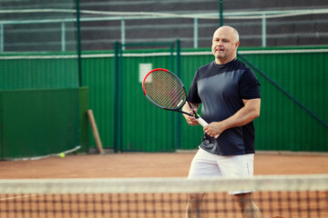 An aged man plays tennis on the court. Active lifestyle and health.