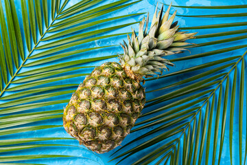  Pineapple and tropical palm leaves on blue cement background.Top view