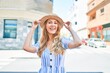 © Krakenimages.com - Young beautiful blonde woman on vacation wearing summer hat smiling happy. Standing with smile on face at street of city.