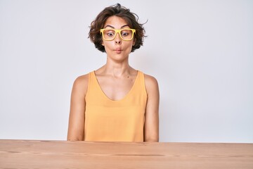 Sticker - Young hispanic woman wearing casual clothes and glasses sitting on the table making fish face with lips, crazy and comical gesture. funny expression.