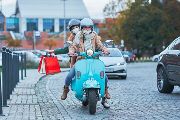 Two women wearing masks and holding shopping bags on scooter