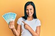 Beautiful hispanic woman holding 100 brazilian real banknotes smiling happy pointing with hand and finger