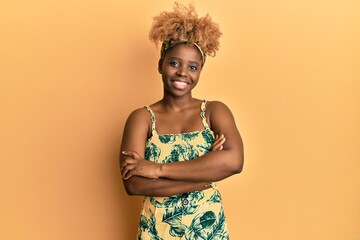 Young african woman with afro hair wearing summer dress happy face smiling with crossed arms looking at the camera. positive person.