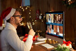 © insta_photos - Happy young man wearing santa hat drinking champagne talking to friends on virtual video call meeting celebrate New Year party in holiday distance online conference chat together on computer at home.