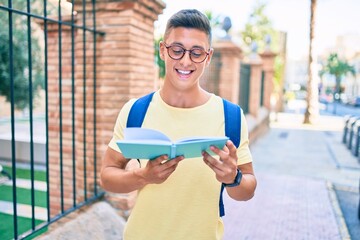 Wall Mural - Young hispanic student smiling happy reading book standing at street of city