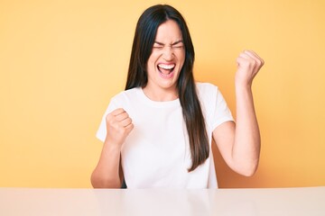 Sticker - Young caucasian woman sitting at the desk wearing casual white tshirt celebrating surprised and amazed for success with arms raised and eyes closed