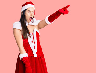 Poster - Young beautiful caucasian woman wearing santa claus costume pointing with finger surprised ahead, open mouth amazed expression, something on the front