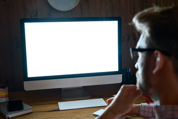 Over shoulder view at business man using desktop computer looking at mock up white blank screen monitor for advertising working late e learning online on website, watching webinar at home office.