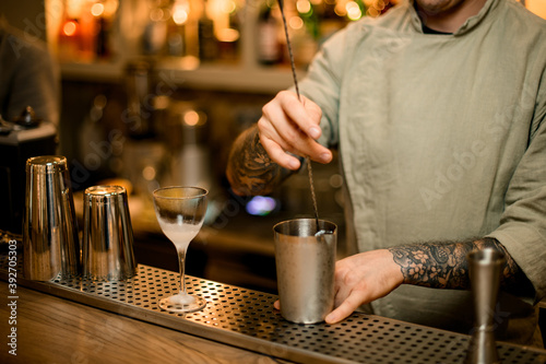 barman holding long bar spoon and stirring cocktail in mixing cup