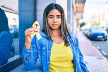 Young Latin Woman With Serious Expression Holding Yellow Ribbon At City.