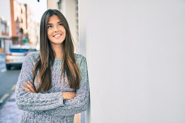 Poster - Young beautiful hispanic girl smiling happy leaning on the wall at the city.