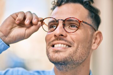 Young hispanic businessman smiling happy touching his glasses at the city.