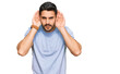 © Krakenimages.com - Young hispanic man wearing casual clothes trying to hear both hands on ear gesture, curious for gossip. hearing problem, deaf