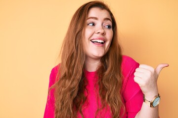 Poster - Young redhead woman wearing casual clothes pointing thumb up to the side smiling happy with open mouth