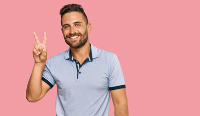 Handsome man with beard wearing casual clothes showing and pointing up with fingers number two while smiling confident and happy.