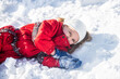 Girl lying on the snow. Funny little child having fun in winter park during snowfall.