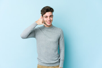 Wall Mural - Young caucasian man isolated on blue background showing a mobile phone call gesture with fingers.