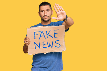 Canvas Print - Handsome man with tattoos holding fake news banner with open hand doing stop sign with serious and confident expression, defense gesture