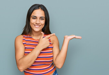 Young brunette woman wearing casual clothes amazed and smiling to the camera while presenting with hand and pointing with finger.