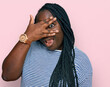 © Krakenimages.com - Young black woman with braids wearing casual clothes peeking in shock covering face and eyes with hand, looking through fingers with embarrassed expression.