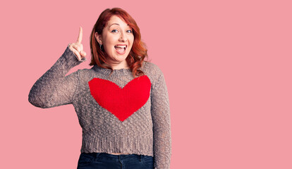 Poster - Young beautiful redhead woman wearing casual heart sweater pointing finger up with successful idea. exited and happy. number one.