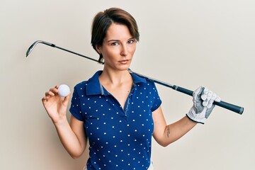 Wall Mural - Young brunette woman with short hair holding ball and golf club clueless and confused expression. doubt concept.