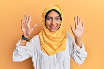 Sticker - Young brunette arab woman wearing traditional islamic hijab scarf showing and pointing up with fingers number ten while smiling confident and happy.