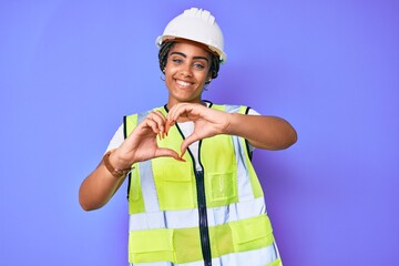 Sticker - Young african american woman with braids wearing safety helmet and reflective jacket smiling in love showing heart symbol and shape with hands. romantic concept.