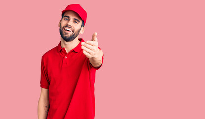 Young handsome man with beard wearing delivery uniform smiling friendly offering handshake as greeting and welcoming. successful business.