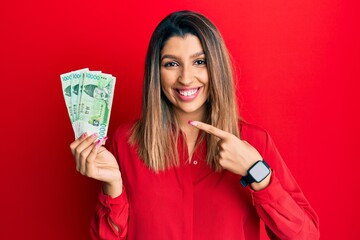 Poster - Beautiful brunette woman holding 10000 south korean won banknotes smiling happy pointing with hand and finger