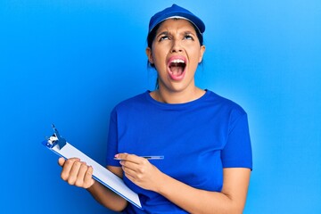 Sticker - Beautiful brunette woman wearing courier uniform holding clipboard angry and mad screaming frustrated and furious, shouting with anger looking up.