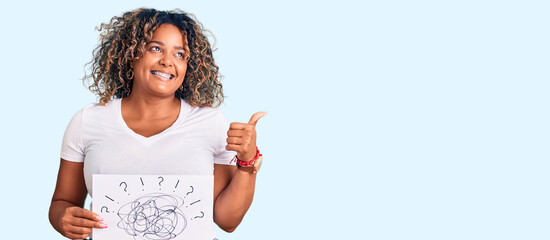 Young african american plus size woman holding scribble draw pointing thumb up to the side smiling happy with open mouth