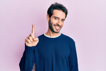 Sticker - Young hispanic man wearing casual clothes smiling with an idea or question pointing finger up with happy face, number one