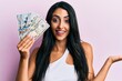 © Krakenimages.com - Beautiful hispanic woman holding dollars celebrating achievement with happy smile and winner expression with raised hand