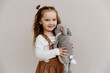 © Елена Лавринович - portrait of a little cute girl with a toy in her hands on a beige background. Three year old child smiling and looking at the camera. handmade knitted toy hare