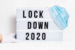 Hands in white gloves hold Light box with message lockdown 2020 and Surgical protective mask. Word of the Year 2020 is lockdown.