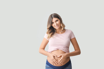 Canvas Print - Beautiful pregnant woman making heart with her hands on light background