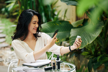 Pretty smiling young Asian businesswoman taking photos of cosmetics for her online store