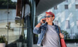© Halfpoint - Senior woman with purple pink hair and smartphone walking outdoors in city or town.