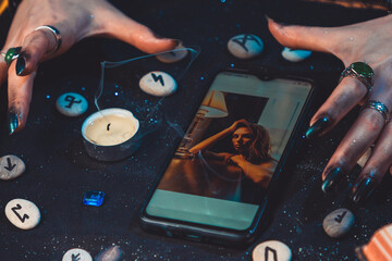 Magic and online fortune telling. The hands of a witch and fortune teller cast a spell over a photo on a smartphone. Close up