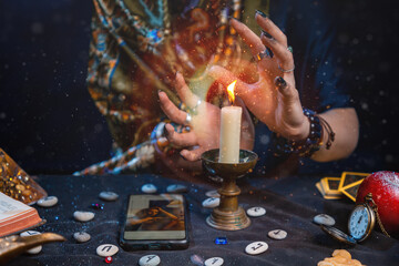 Wall Mural - Astrology and online divination. A fortune teller does online fortune telling on photos from a smartphone. There are magic items on the table. Close-up of hands and candles.