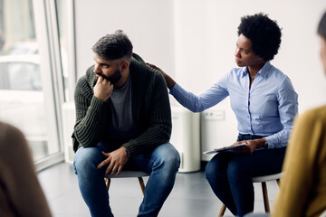 Black female therapist supporting a man who is talking abut his issues during group meeting.