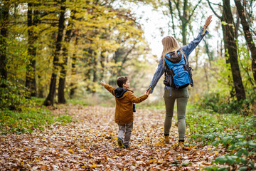 Happy mother and son are hiking in forest.