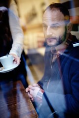 Poster - Thoughtful man sitting in cafeteria. Photographed through window.