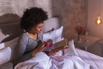 Sticker - Woman lying in bed reading a book and drinking tea