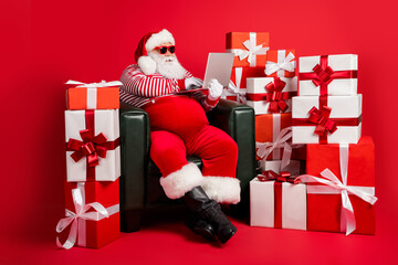 Wall Mural - Photo of santa claus sit armchair use netbook wear x-mas costume suspenders cap eyewear isolated decorated red color background