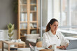 © Seventyfour - Portrait of elegant young woman looking at laptop screen while enjoying work in white office interior, copy space
